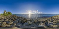 a picture taken from the water and of rocks, in the sun, and a city with tall buildings and clouds in the sky