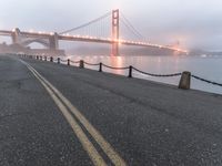 an empty street beside the water and a bridge with fog covering it from sun and fog