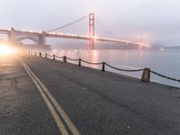 an empty street beside the water and a bridge with fog covering it from sun and fog