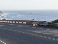 a woman riding a scooter across a road near the ocean and cliffs on a foggy day