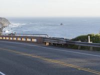 a woman riding a scooter across a road near the ocean and cliffs on a foggy day