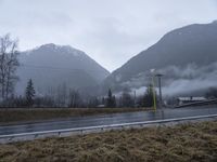 an asphalt road near trees and mountains on a foggy day with water coming from the tops