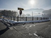 a road covered in snow next to a fence and mountains in the background under a blue sky