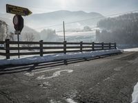 a road covered in snow next to a fence and mountains in the background under a blue sky