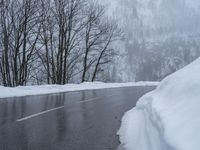 an asphalt road with snow covered trees lining the sides of it and on top of the road is a slope with a road sign near by the road