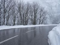 an asphalt road with snow covered trees lining the sides of it and on top of the road is a slope with a road sign near by the road