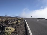 a road near the mountain side in the foggy sun day, and on the opposite bank are hills