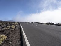 a road near the mountain side in the foggy sun day, and on the opposite bank are hills