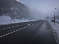 a foggy highway with snow on the ground and lights in front of it and a mountain