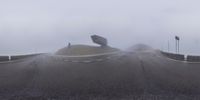 someone standing on a hill while holding up umbrellas in the rain, under a foggy sky