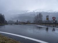 wet roadway with highway signs, snowy mountain range in background, in motion of raining