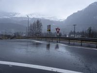 wet roadway with highway signs, snowy mountain range in background, in motion of raining