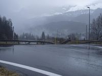 wet roadway with highway signs, snowy mountain range in background, in motion of raining