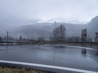 wet roadway with highway signs, snowy mountain range in background, in motion of raining