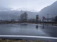 wet roadway with highway signs, snowy mountain range in background, in motion of raining