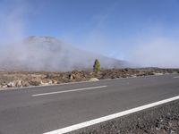 a road near the mountain side in the foggy sun day, and on the opposite bank are hills