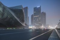 cars drive down a foggy street with tall buildings behind it at night in front of tall towers