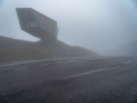 a very large building in the middle of the foggy hillside of a road