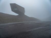 a very large building in the middle of the foggy hillside of a road