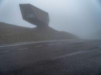 a very large building in the middle of the foggy hillside of a road