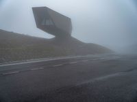 a very large building in the middle of the foggy hillside of a road