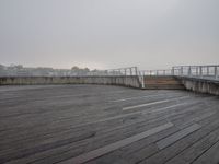 wooden boardwalk on the seafront at the foggy day in a city area with an observation point looking down over a lake