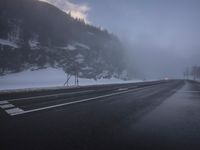 a foggy roadway with snow and some traffic lights on it in the distance is mountains