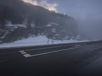 a foggy roadway with snow and some traffic lights on it in the distance is mountains
