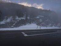 a foggy roadway with snow and some traffic lights on it in the distance is mountains