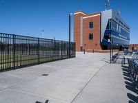 a baseball field with an empty field and seating by a fence and building behind the baseball stadium