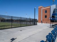 a baseball field with an empty field and seating by a fence and building behind the baseball stadium