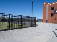 a baseball field with an empty field and seating by a fence and building behind the baseball stadium