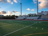 a sports field with a goalie bench in it and buildings in the background during sunset