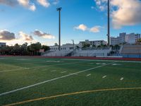 a sports field with a goalie bench in it and buildings in the background during sunset