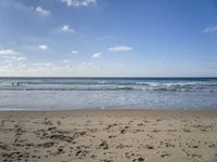 footprints are seen on the sand at the beach as the waves move in nearby, near by