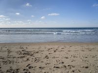 footprints are seen on the sand at the beach as the waves move in nearby, near by