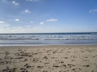 footprints are seen on the sand at the beach as the waves move in nearby, near by