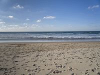 footprints are seen on the sand at the beach as the waves move in nearby, near by