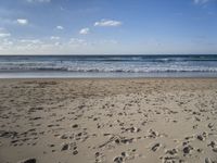 footprints are seen on the sand at the beach as the waves move in nearby, near by