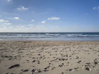 footprints are seen on the sand at the beach as the waves move in nearby, near by