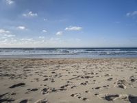 footprints are seen on the sand at the beach as the waves move in nearby, near by