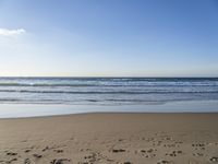 footprints on the sandy beach as the sun shines brightly above the sea foams