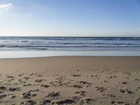 footprints on the sandy beach as the sun shines brightly above the sea foams