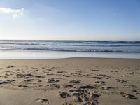 footprints on the sandy beach as the sun shines brightly above the sea foams