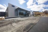 ford car dealership at the corner of a road near an intersection with mountains and clouds