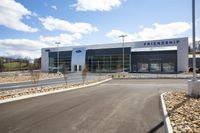 the front of a ford dealership surrounded by rock and grass near a parking lot