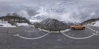 an orange pick up truck parked in front of a mountain range in the distance with snow