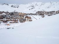 skiers and snow boarders stand at the base of a snowy mountain in front of town