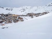 skiers and snow boarders stand at the base of a snowy mountain in front of town