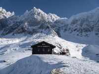 there are snow - covered hills and mountains behind the small hut that the skiers sit in